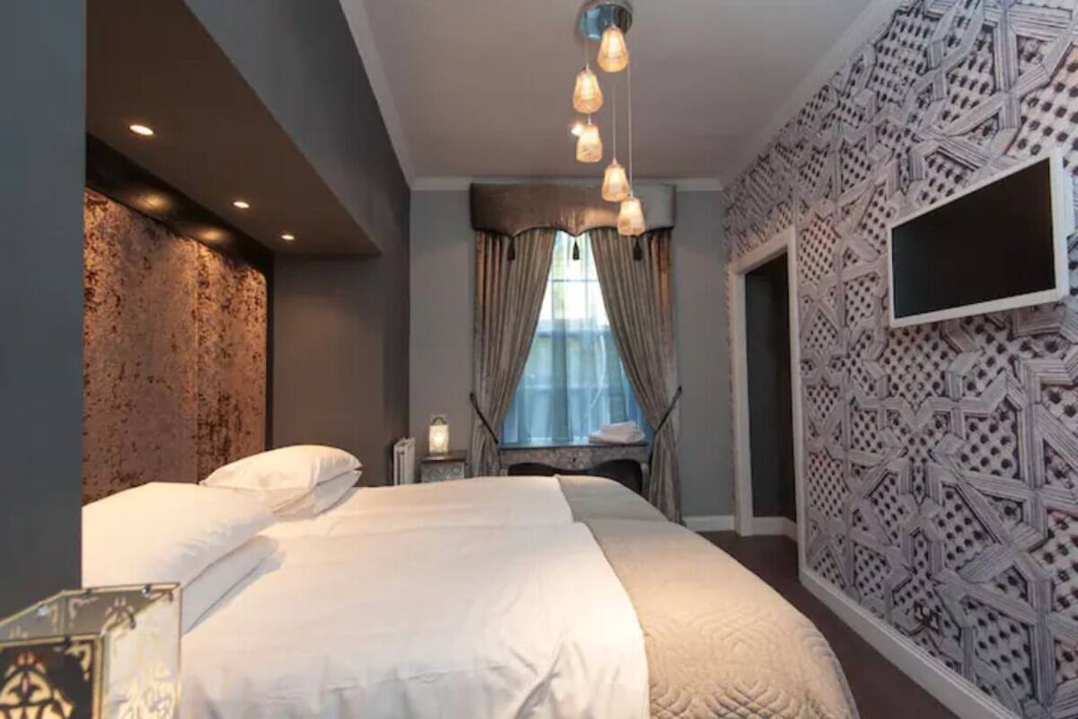 A modern hotel room with a large bed, a TV mounted on the wall, and a patterned wall design.