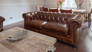 Un salon spacieux avec un canapé en cuir, une table basse en bois et un coin repas agrémenté d’un lustre.