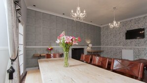 Un espace repas avec une longue table en bois, des chaises en cuir, un vase de fleurs et un lustre.