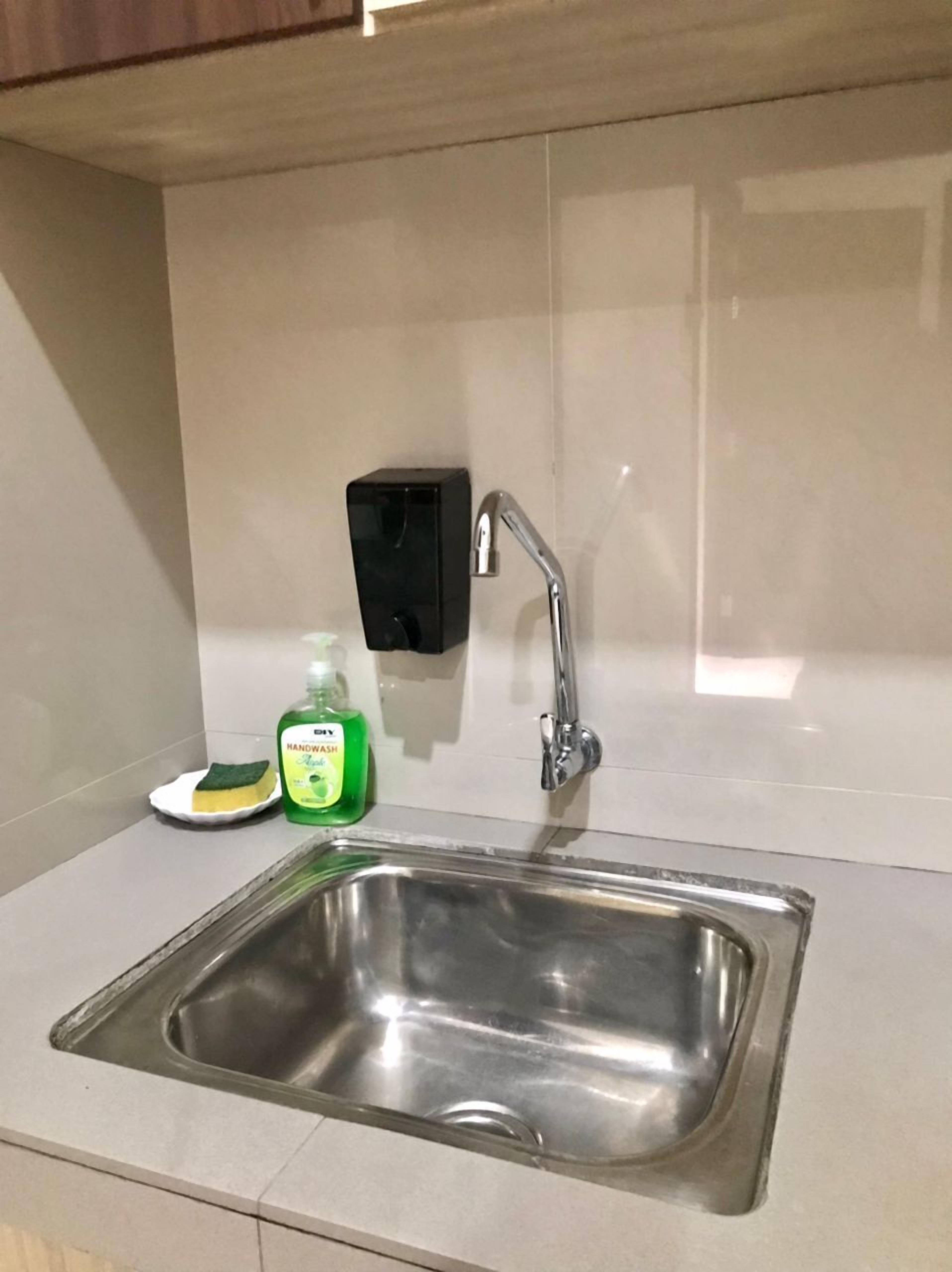 Ein Spülbecken aus Edelstahl mit einem modernen Wasserhahn, einer Seifenspender und einem Schwamm auf der Arbeitsplatte.