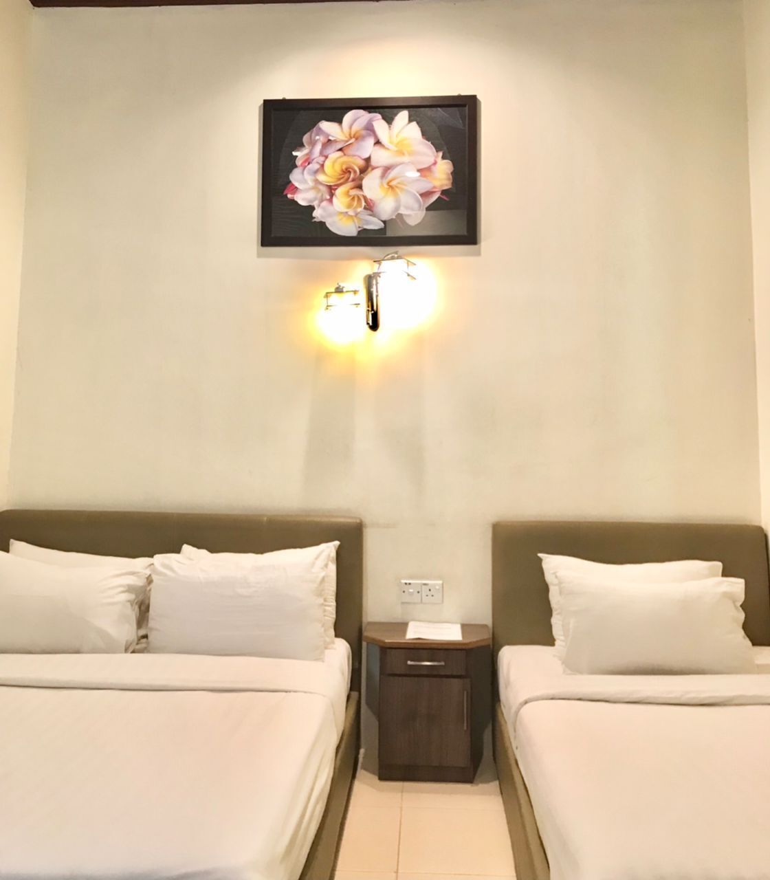 Een hotelkamer met twee bedden, een nachtkastje, een wandlamp en een lijst met bloemwerk.