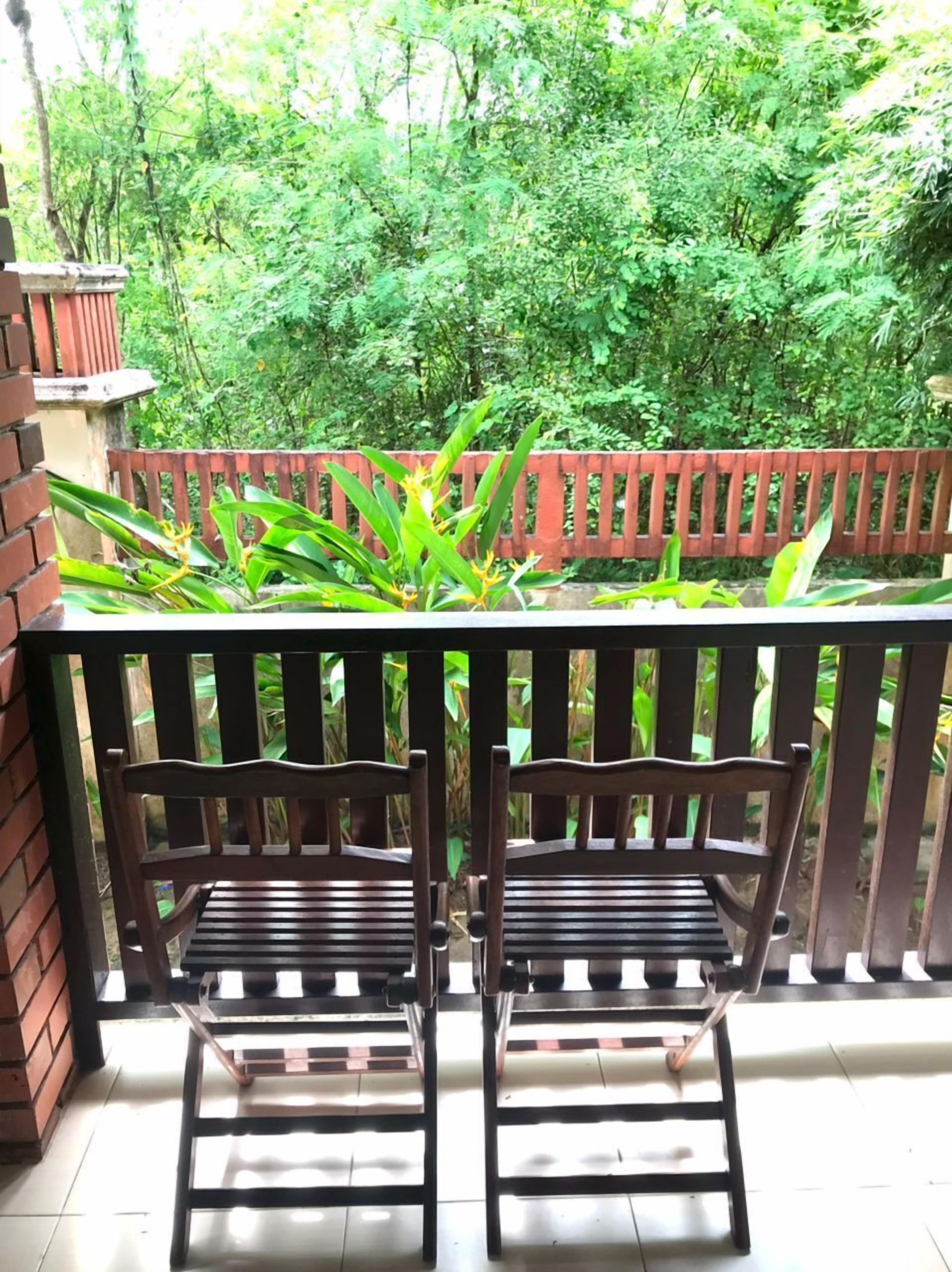 Two wooden chairs with slatted seats and backs, positioned on a tiled floor with a red wooden railing behind them.