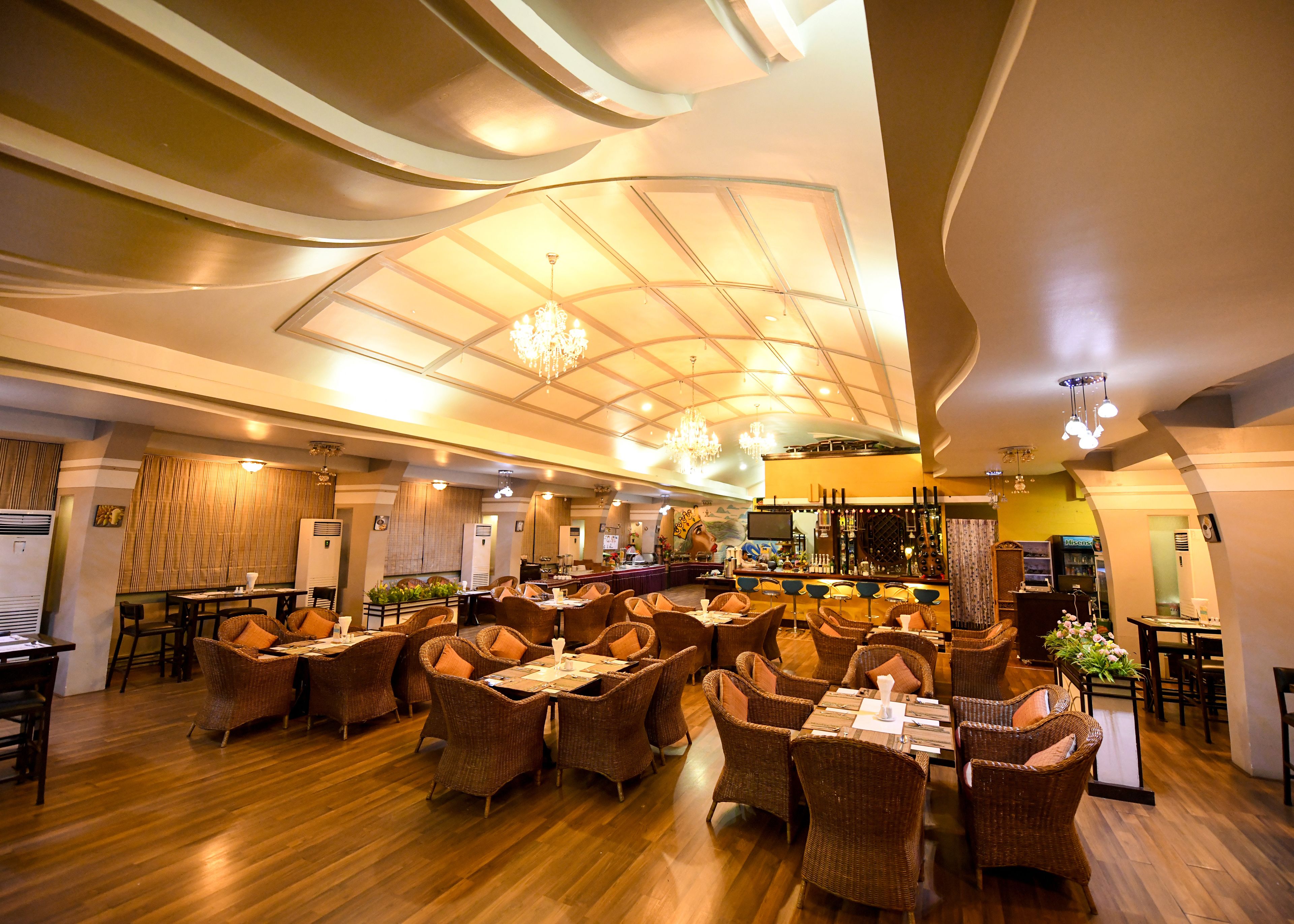 Un restaurant spacieux avec de hauts plafonds, des lustres modernes et des meubles en osier.