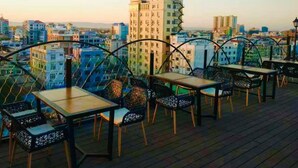 Una terraza en la azotea con mesas y sillas, con vistas a un paisaje urbano con varios edificios.