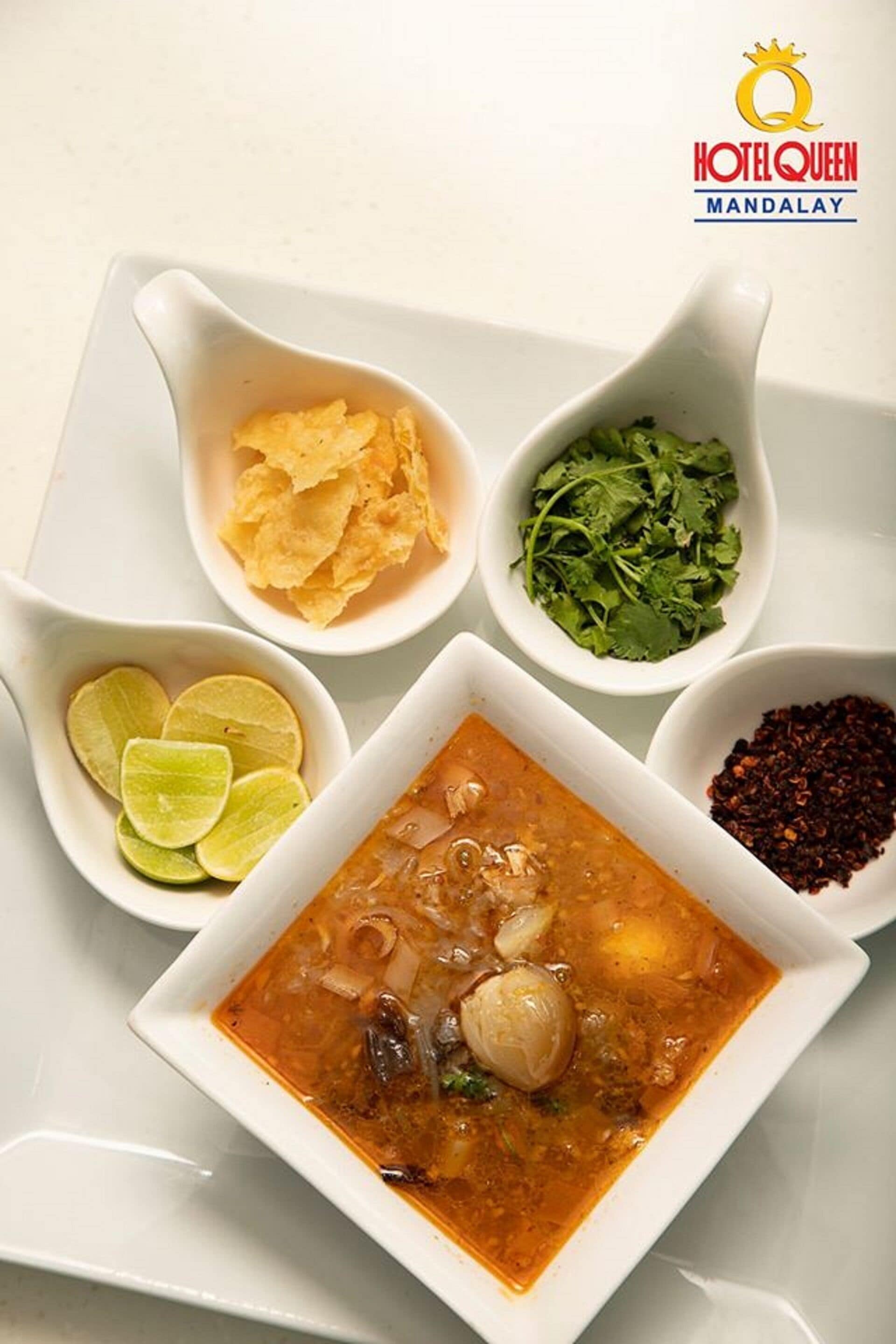 Eine Schüssel Suppe mit Limettenstückchen, eine Schüssel Chips, eine Schüssel Koriander und eine Schüssel Chiliflocken.