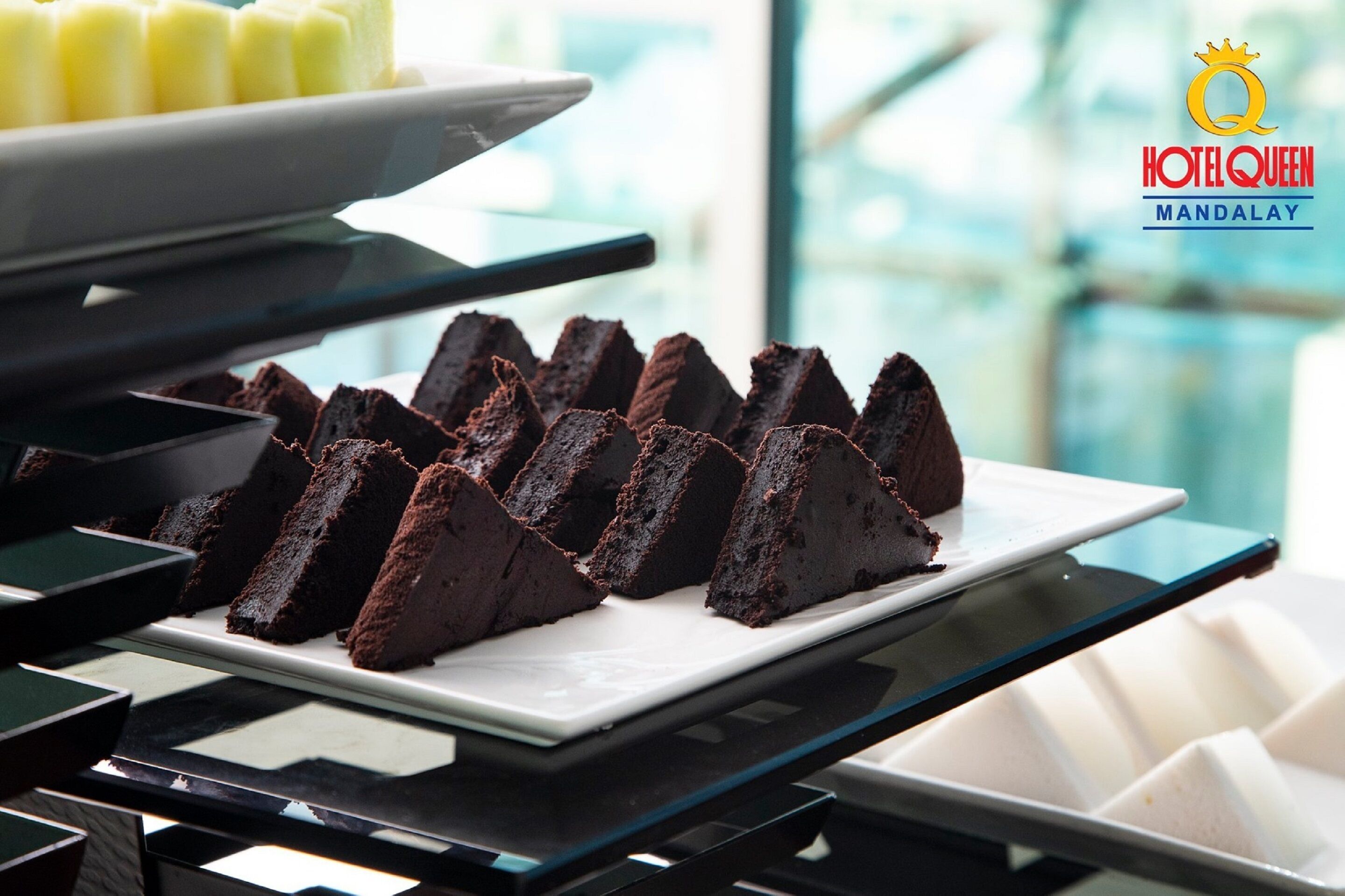 A dessert display with chocolate cake slices on a white plate, a white dessert tray, and a glass dessert stand.