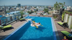 Una piscina en la azotea con un flotador con forma de cisne, sillas de descanso y vistas a la ciudad.