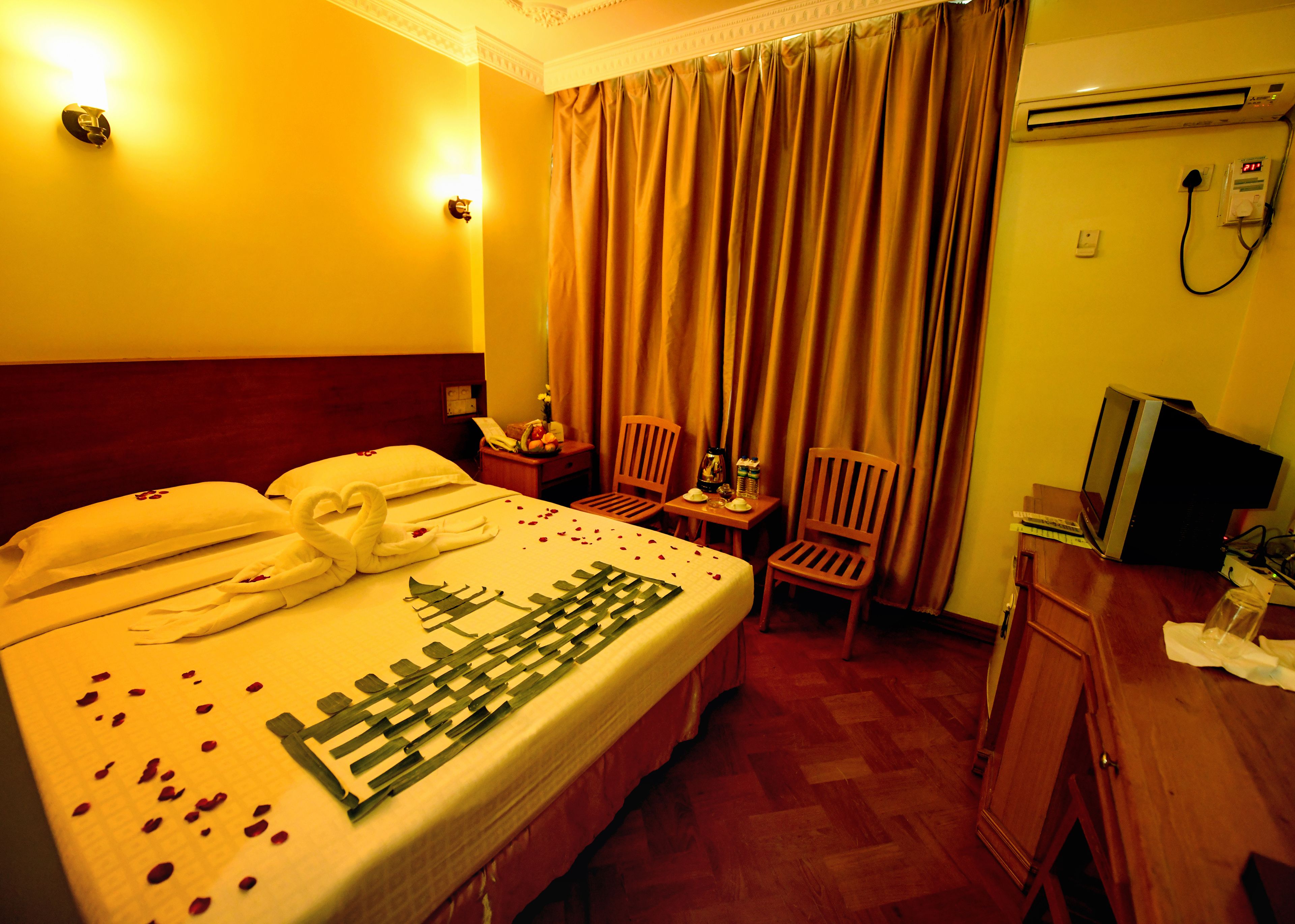 A hotel room with a neatly made bed, a wooden chair, a desk with a computer, and a window with curtains.