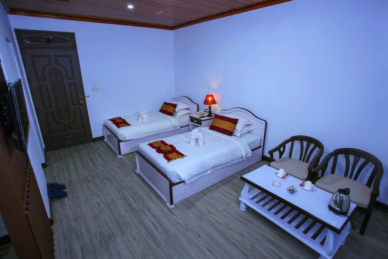 A hotel room with two single beds, a small table with tea set, and a wooden door.