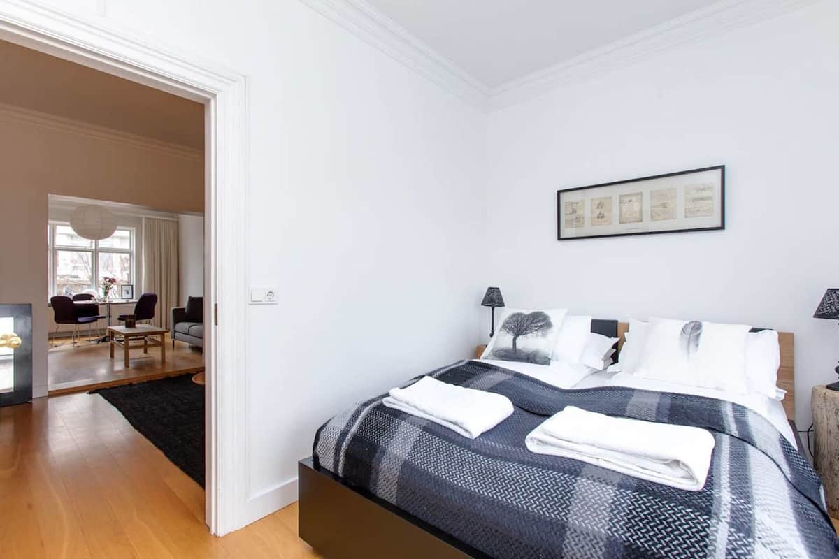 Quarto com cama, mesas de cabeceira, um quadro e vista para a sala de estar.