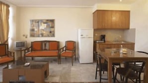 A compact living space with a sofa, chairs, a small table, a refrigerator, and a kitchenette. - Theo Beach Hotel (Rethymnon)