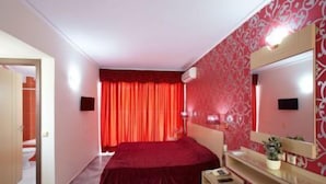 A bedroom with a bed, a bedside table, a mirror, and a red curtain. - Theo Beach Hotel (Rethymnon)