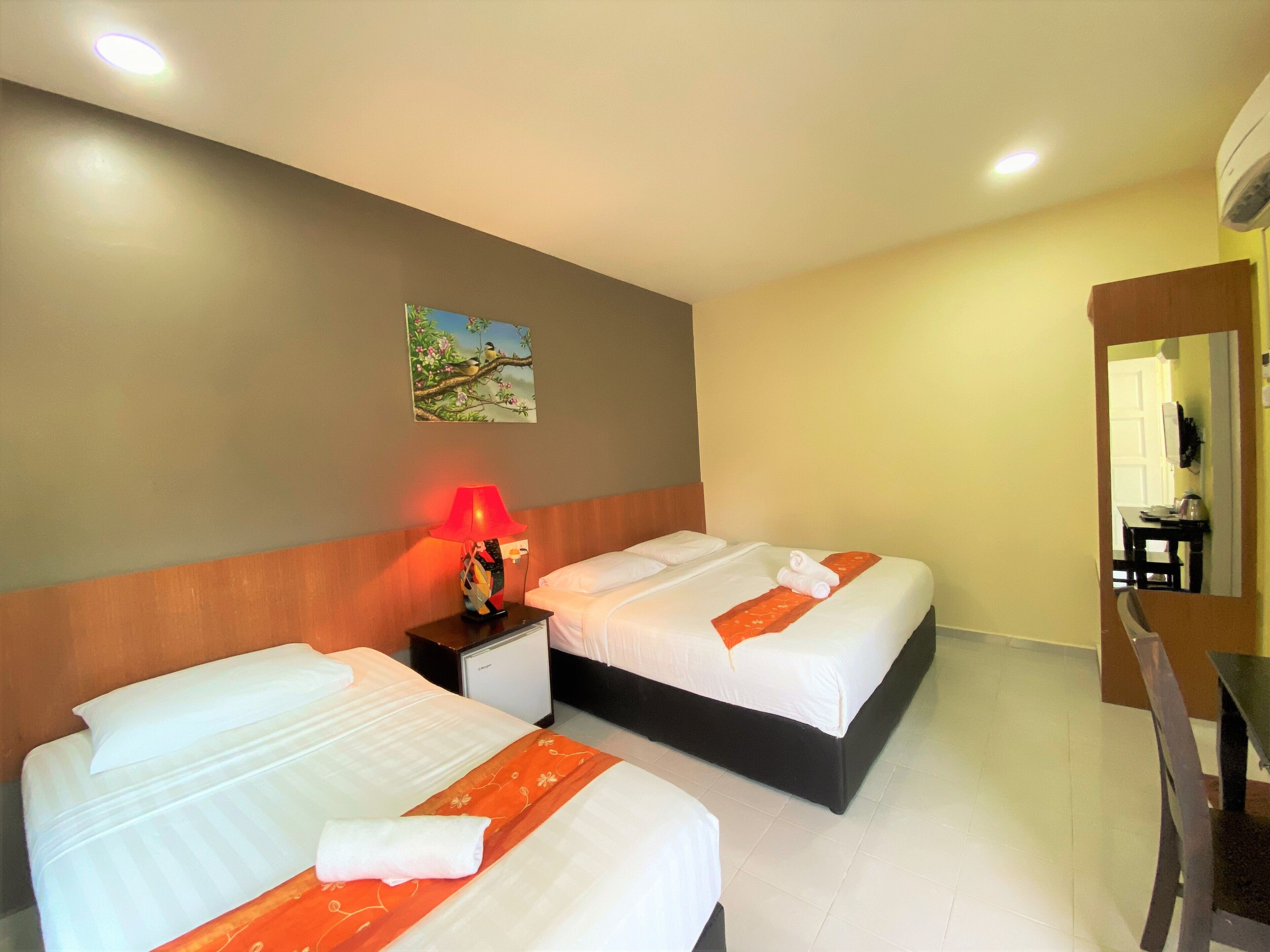 A hotel room with two beds, a nightstand with a lamp, a small table, and a chair.