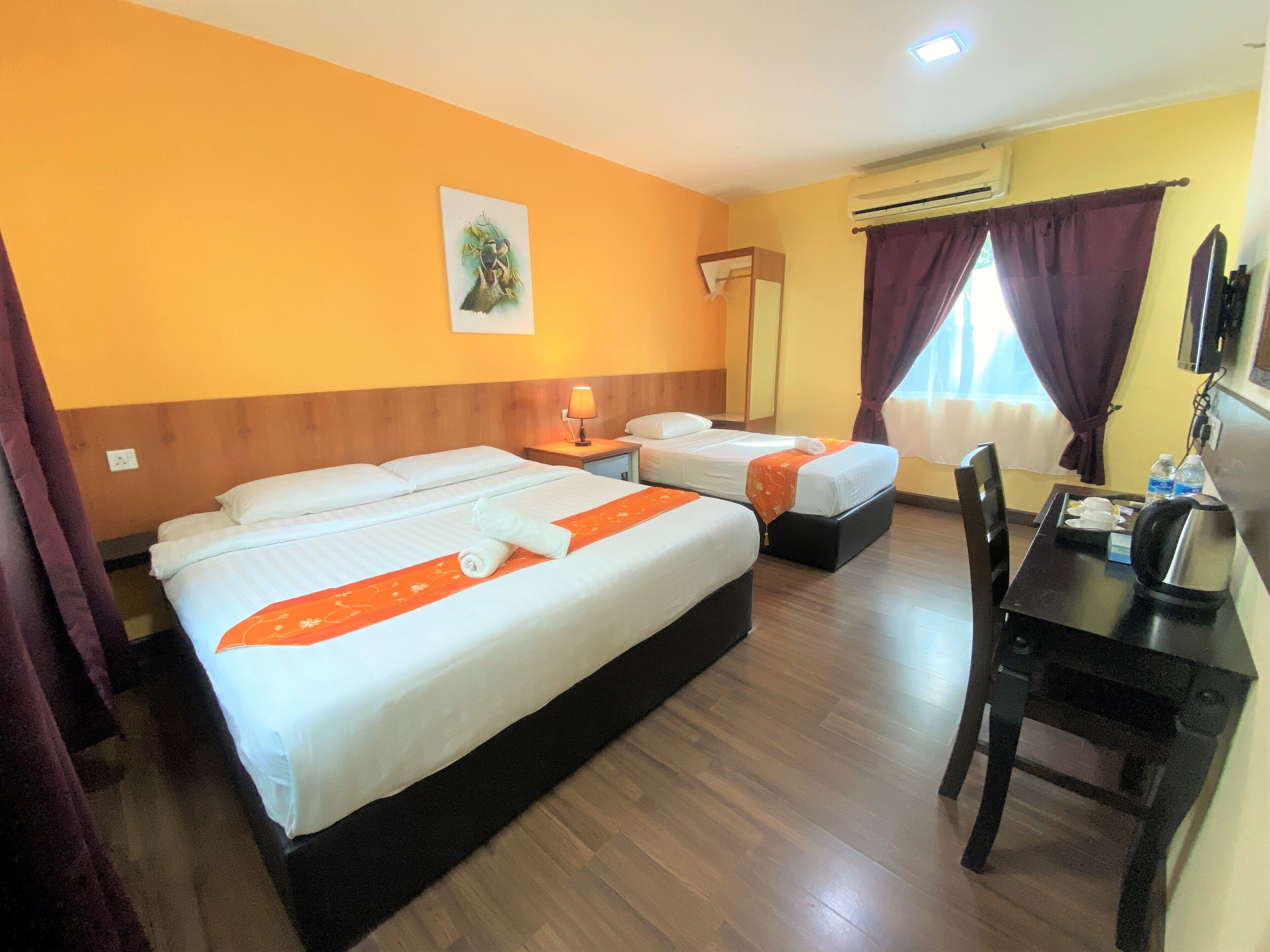 Une chambre d’hôtel avec deux lits, un bureau, une chaise, un appareil de climatisation et une fenêtre avec des rideaux.