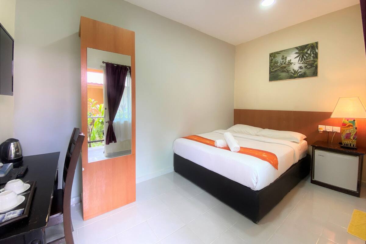 A hotel room with a bed, a desk with a chair, a small table with a lamp, and a painting on the wall.