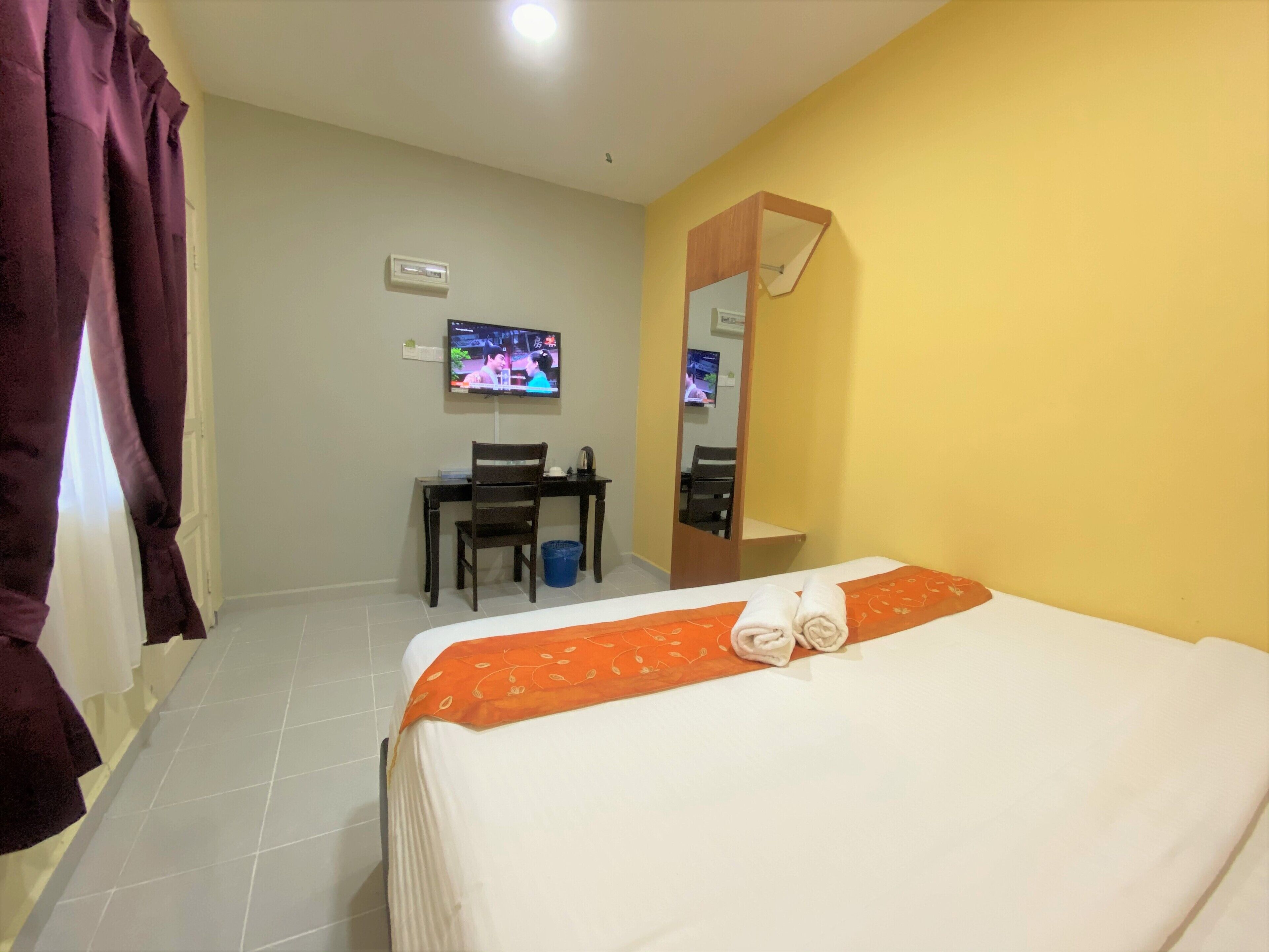 Una habitación de hotel con cama, escritorio, silla, televisor y espejo.