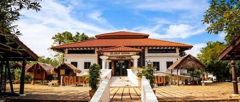 A traditional building with a red-tiled roof, a central entrance with steps, and a sign reading "Selamat Datang Welcome".