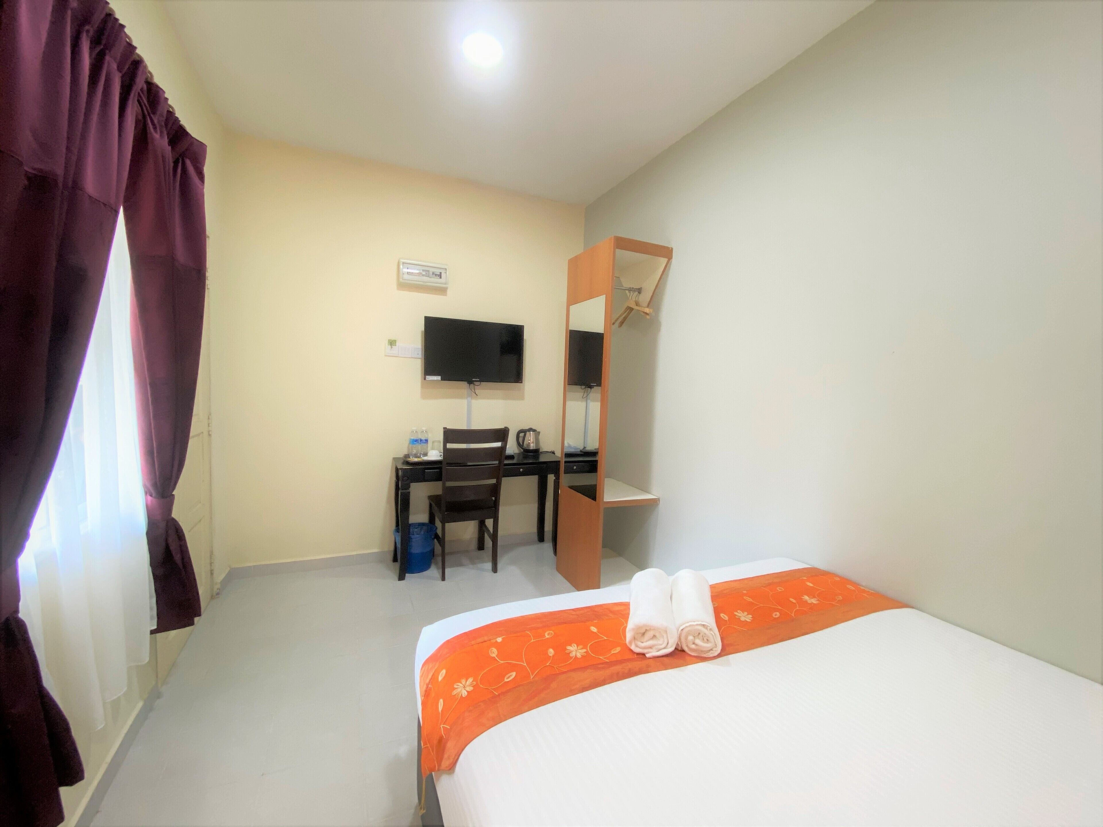 A hotel room with a bed, a desk, a chair, a television, and a mirror.