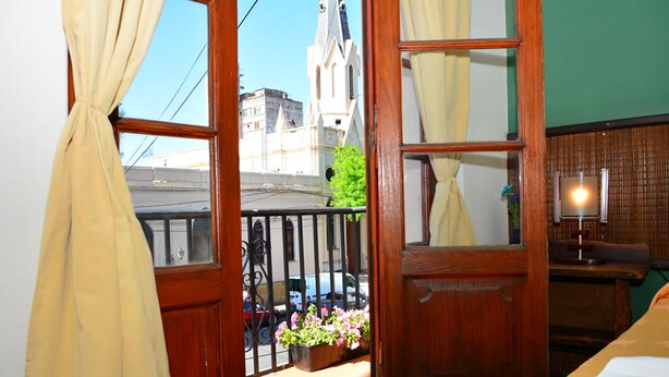 A room with a wooden door, a window with curtains, a small balcony with a railing, and a plant. - Hotel La Giralda (Salta)