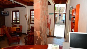 A lobby with a stone pillar, a reception desk with a phone and computer, striped chairs, and a view of the street outside. - Hotel La Giralda (Salta)