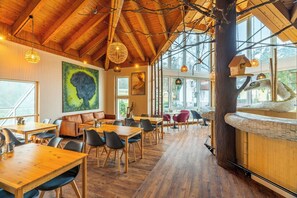 Un comedor amplio con mesas y sillas de madera, ventanas grandes y un techo alto con vigas a la vista.