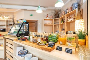 Een ontbijtbuffet met diverse etenswaren en drankjes, waaronder een watermeloen, potten jam en een koffieapparaat.