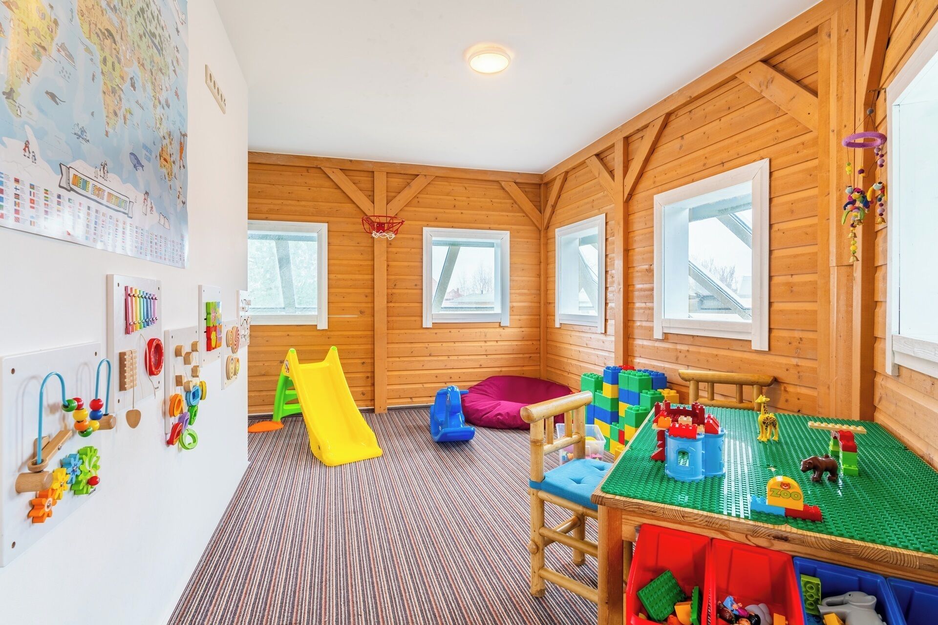 Een houten kinderspeelkamer met een glijbaan, speelmatten en educatief speelgoed.
