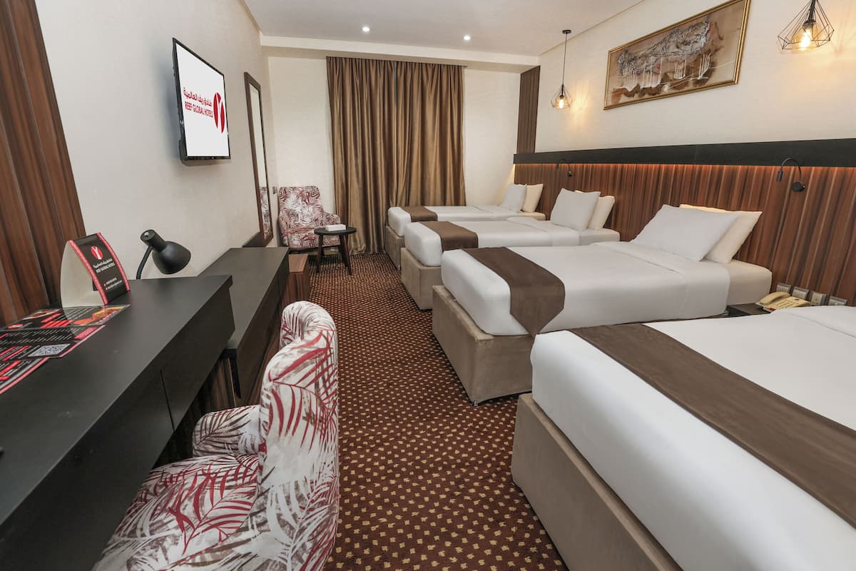 Habitación de hotel con tres camas, un escritorio, una silla y un televisor.