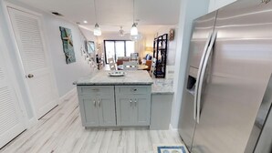 A kitchen with a large island, a stainless steel refrigerator, and a dining area with a view. - The Islands Club (Seven Mile Beach)