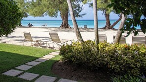 A beachside resort with lounge chairs and tables, a clear view of the ocean, and a pathway leading to the beach. - The Islands Club (Seven Mile Beach)