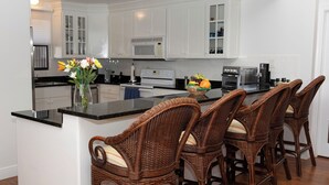 A modern kitchen with white cabinetry, a black countertop, and a central island with wicker chairs. - The Islands Club (Seven Mile Beach)