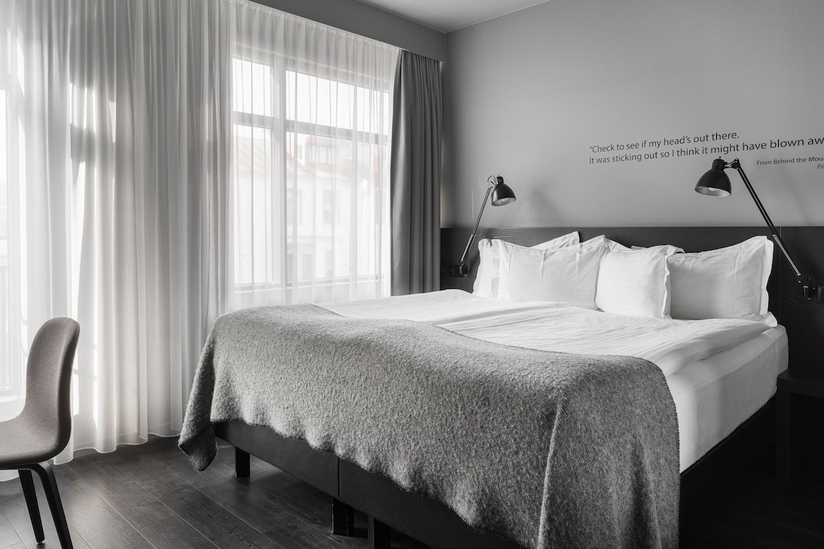 Habitación de hotel moderna con una cama grande, una silla y una pared con una cita.