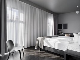 Una habitación de hotel moderna con una cama grande, una mesita de noche, una silla y un televisor montado en la pared.