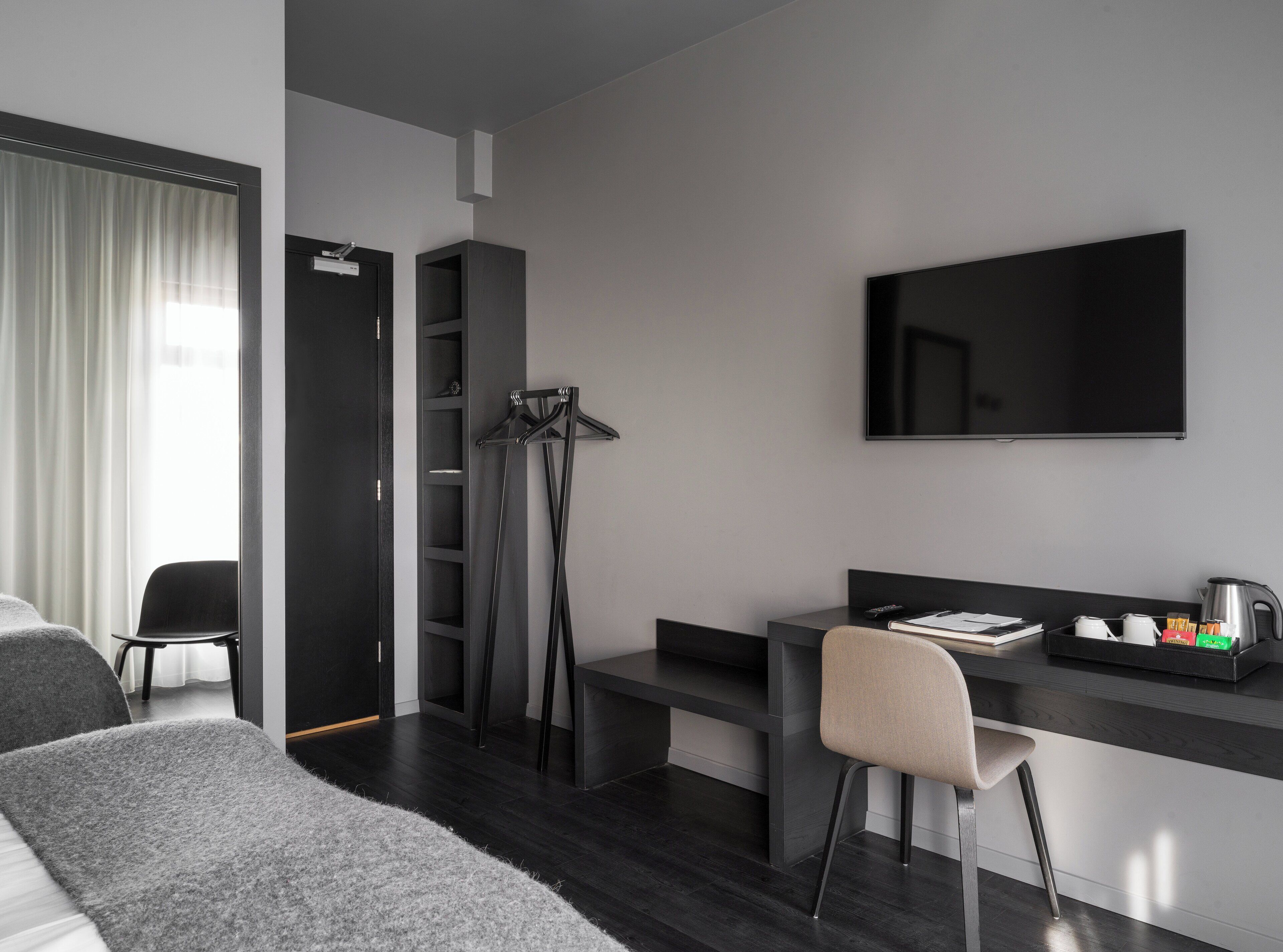 Une chambre d’hôtel moderne équipée d’un lit, d’un bureau, d’une chaise, d’une télévision et d’une armoire.