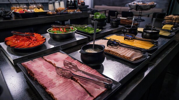 Un bufé con diversos alimentos, incluyendo carne en rodajas, verduras y queso.