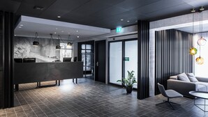 Ein moderner Empfangsbereich mit einer Rezeption, einer Sitzecke mit Sofa und Sesseln sowie einer Zimmerpflanze.