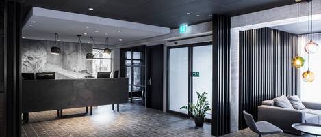 Una moderna zona de recepción con mostrador, un área de estar con sofá y sillones, y una planta en maceta.
