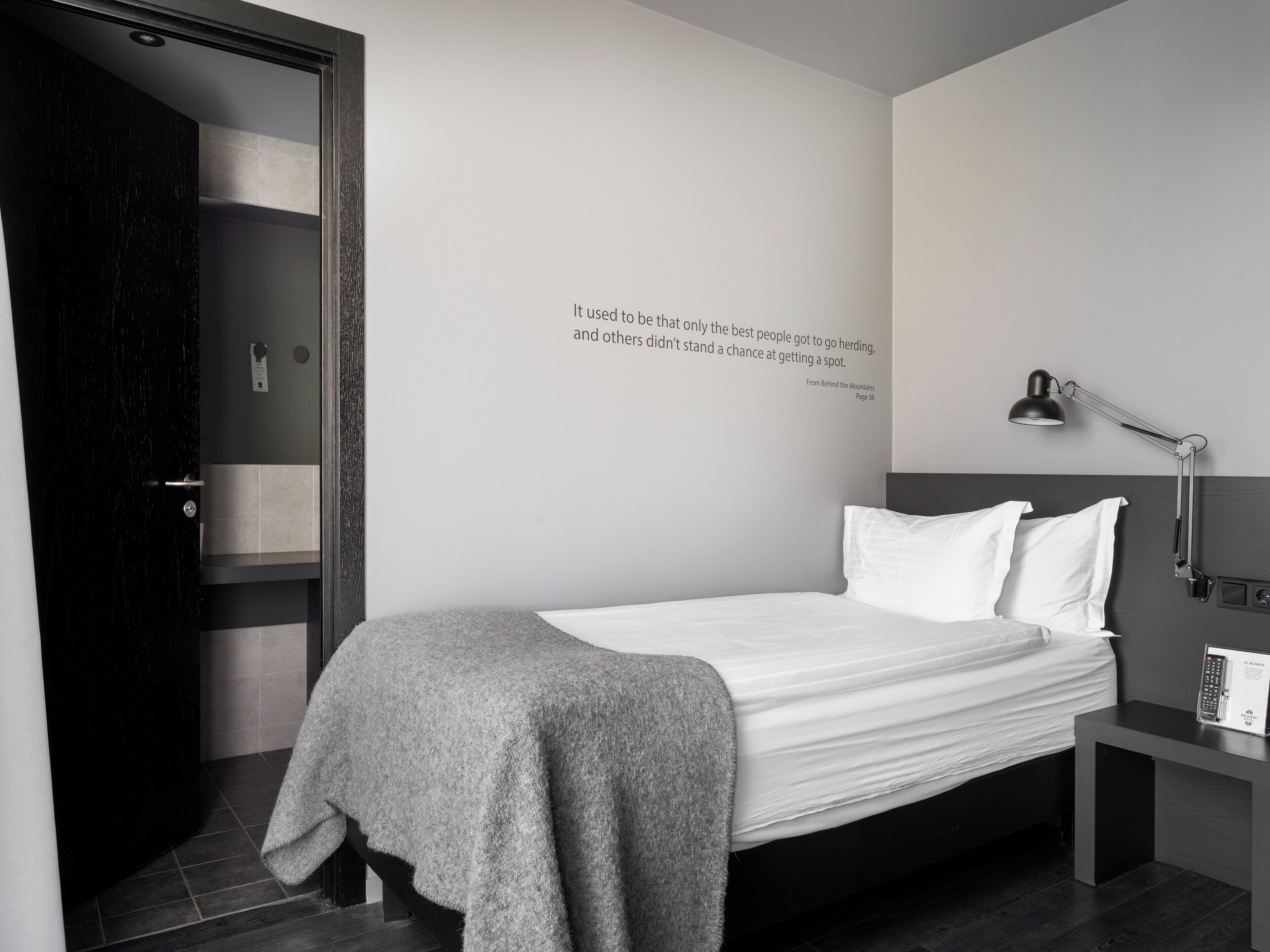 A modern bedroom with a bed, a bedside table, a lamp, and a wall-mounted quote.