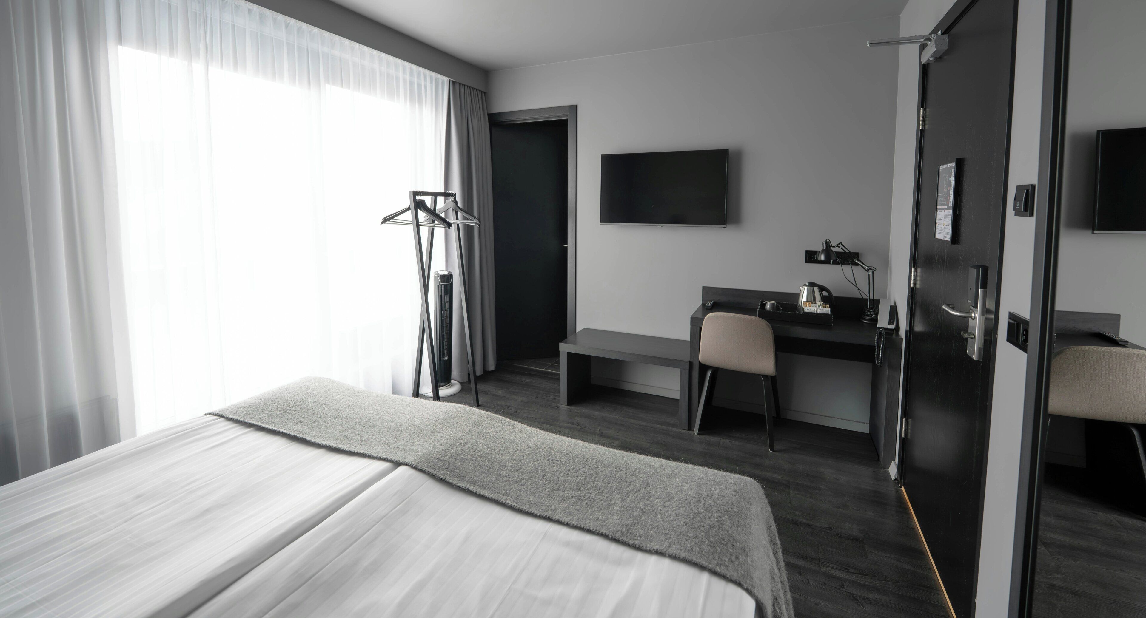 A hotel room with a bed, a desk, a chair, a TV, and a wardrobe.