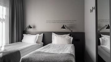 Quarto de hotel com duas camas, um espelho grande e uma frase na parede.