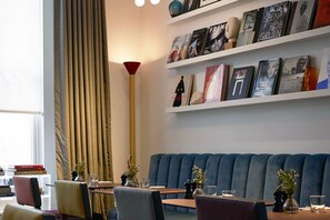 A modern interior with a blue upholstered bench, bookshelves with various books, and a tall red floor lamp. - The Laslett Hotel (London)