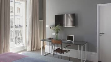 Une chambre d’hôtel avec un lit, un bureau avec un ordinateur portable, une chaise, un téléviseur fixé au mur et une fenêtre avec des rideaux.