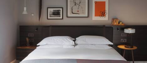 A neatly made bed with white linens, a dark headboard, and a wall with three framed artworks.