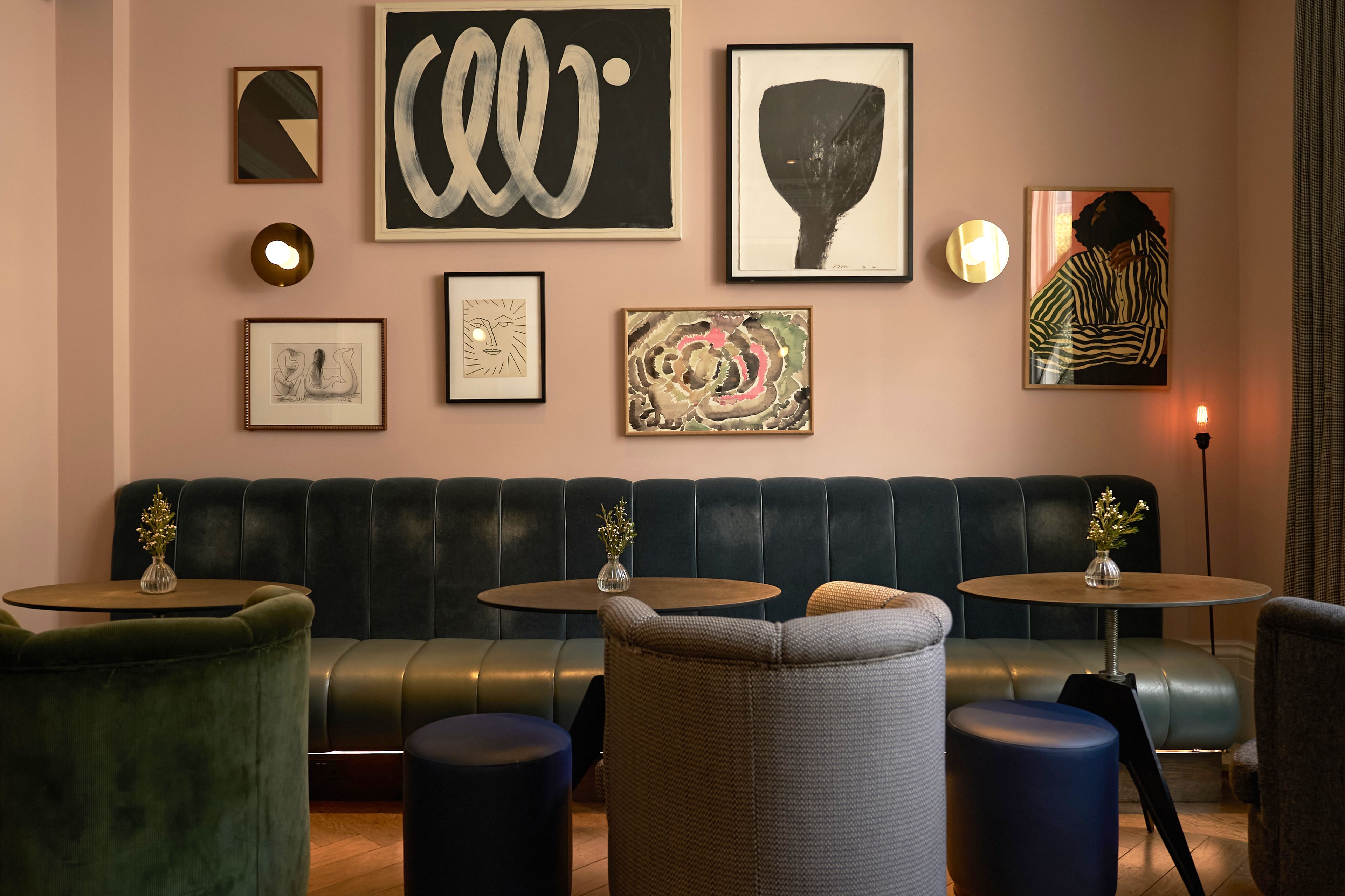 A modern lounge area with a leather sofa, round tables, and various framed artworks on the wall.