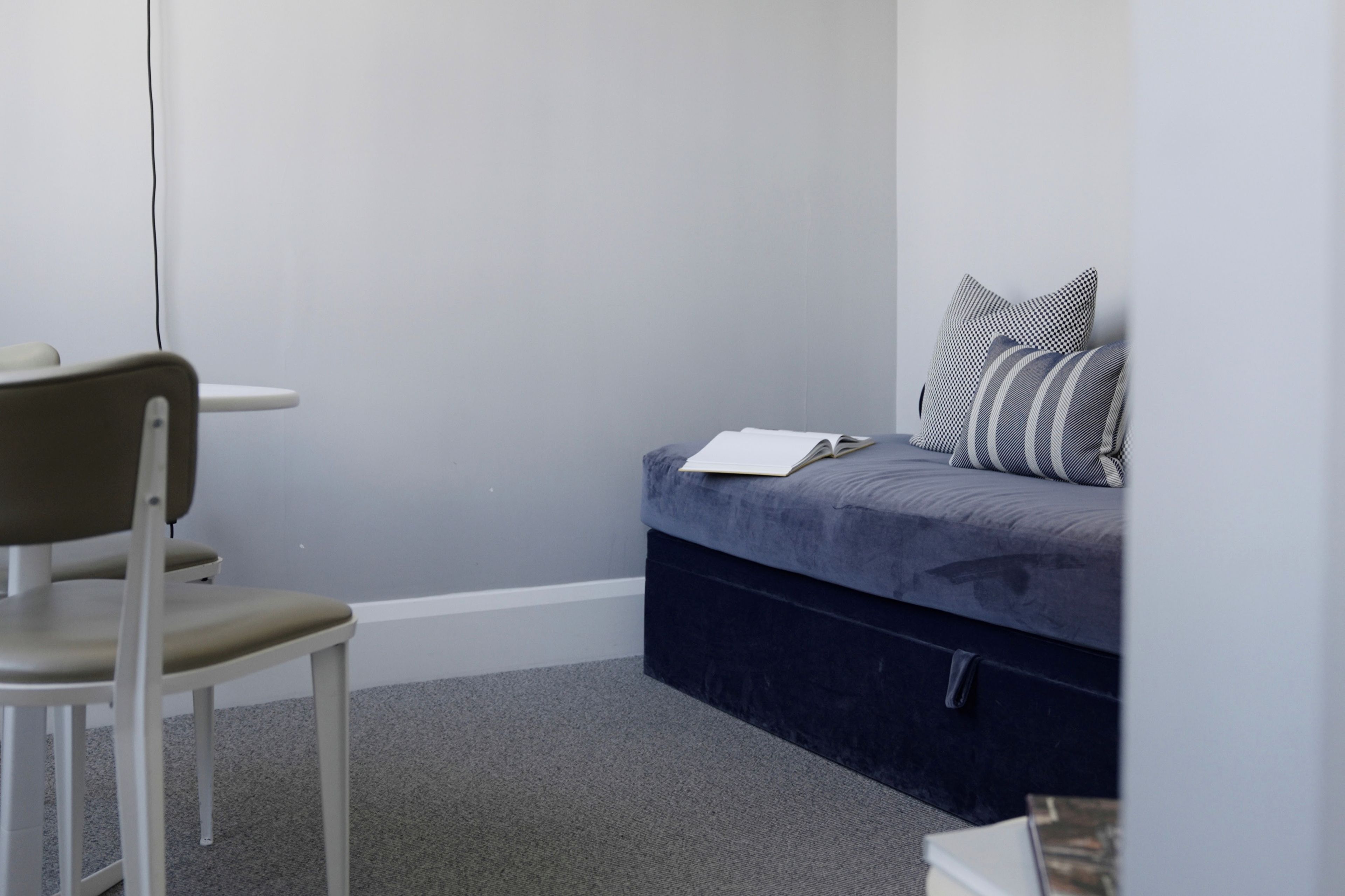 A small room with a grey sofa bed, a white chair, and a grey carpet.