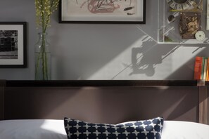 A bedroom with a bed, a framed picture, a vase with flowers, and a wall clock. - The Laslett Hotel (London)