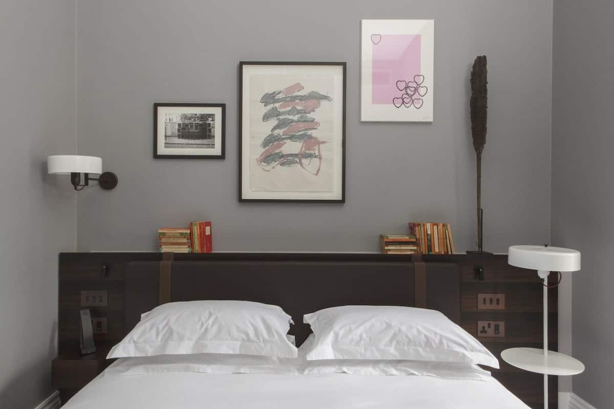 A neatly made bed with white linens, a dark headboard, and a bedside table with books and a lamp.