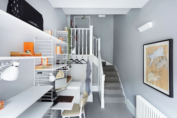 Ein modernes, aufgeräumtes Zimmer mit Schreibtisch, Stuhl und Regalelement. Eine Treppe mit Geländer führt zu einer weiteren Ebene.