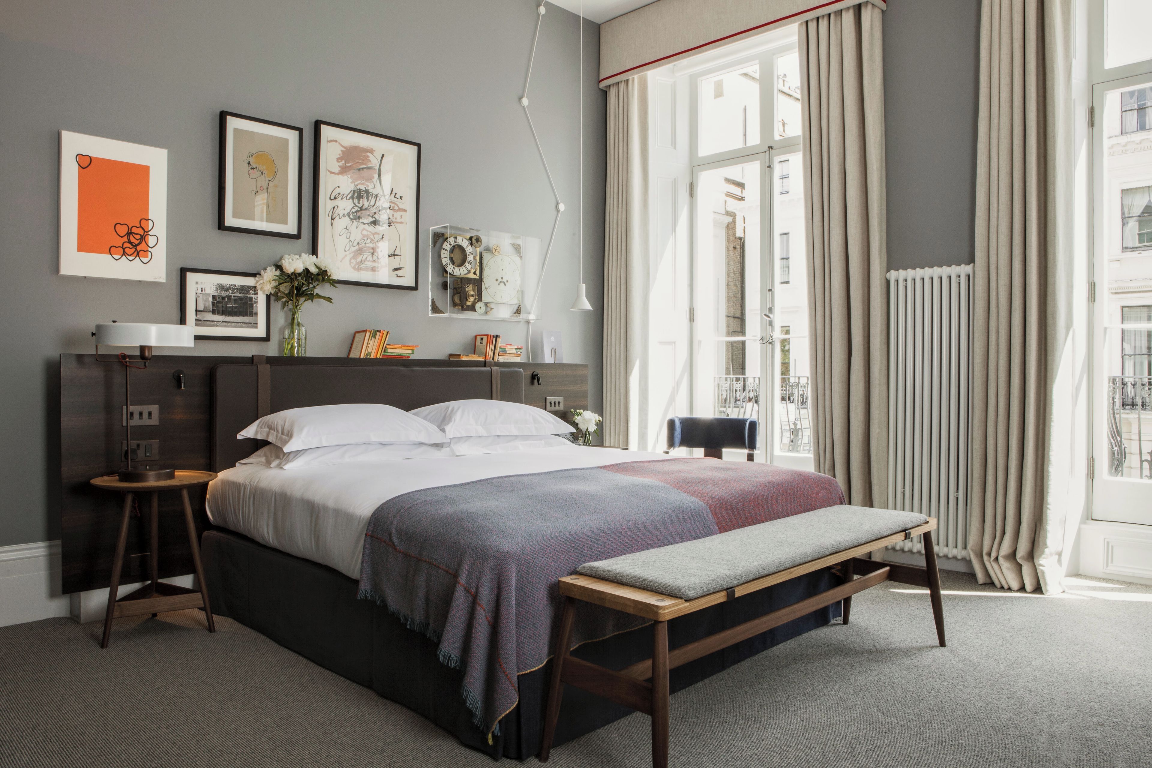 A modern bedroom with a large bed, bedside tables, a bench, and a window with curtains.