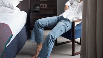 A hotel room with a bed, a chair, a nightstand with a phone, and a carpeted floor.